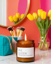 Candle labeled 'YAS QUEEN' with makeup brushes and tulips in the background