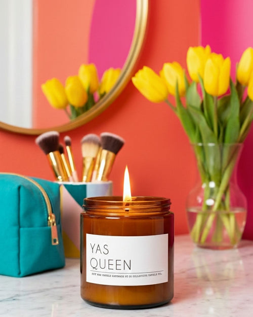 Candle labeled 'YAS QUEEN' with makeup brushes and tulips in the background